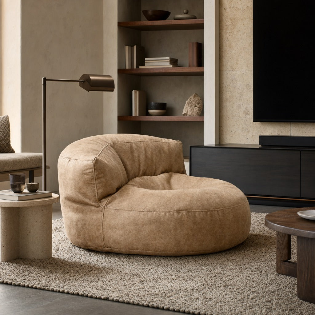 A round, low-profile lounge chair in a warm tan bouclé fabric, styled in a modern living room setting with a shag rug, wooden shelving, and a dark media console.