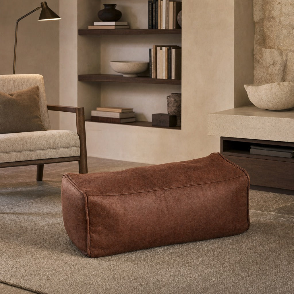 A brown faux-leather rectangular ottoman or bench with rounded corners, placed on a textured beige rug in a modern living room setting.