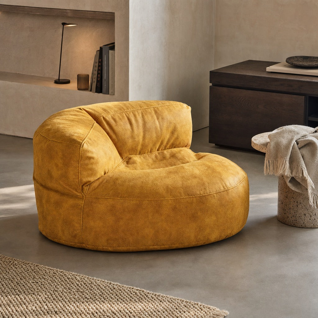 A round, low-profile lounge chair upholstered in textured mustard-yellow fabric, styled in a modern minimalist living room with concrete floors and neutral walls.