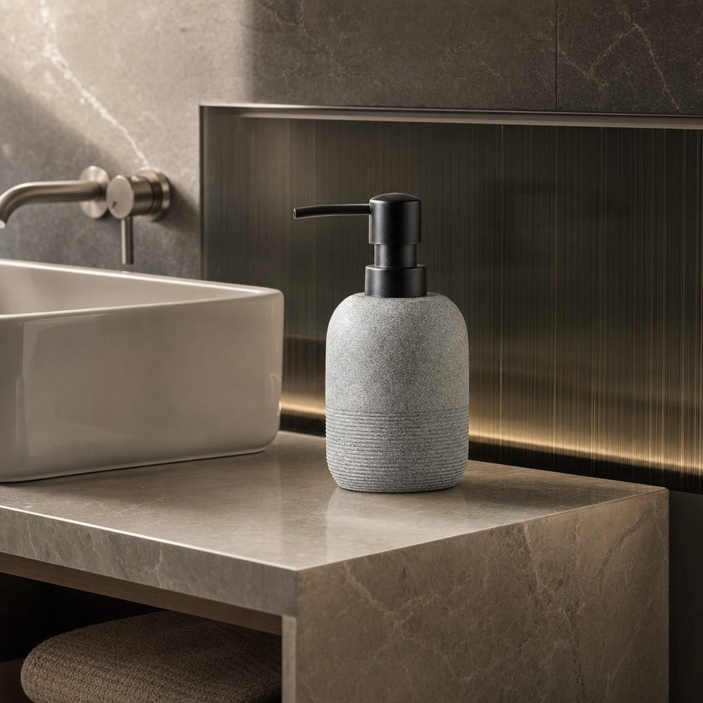 A gray stone-textured soap dispenser with a black pump bottle, styled on a marble bathroom counter next to a white vessel sink.
