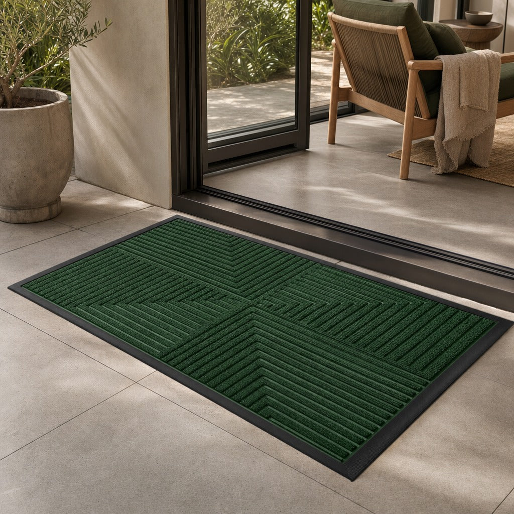 A dark green rectangular doormat with a black border and raised geometric channel pattern, placed at the threshold of a modern patio entryway.