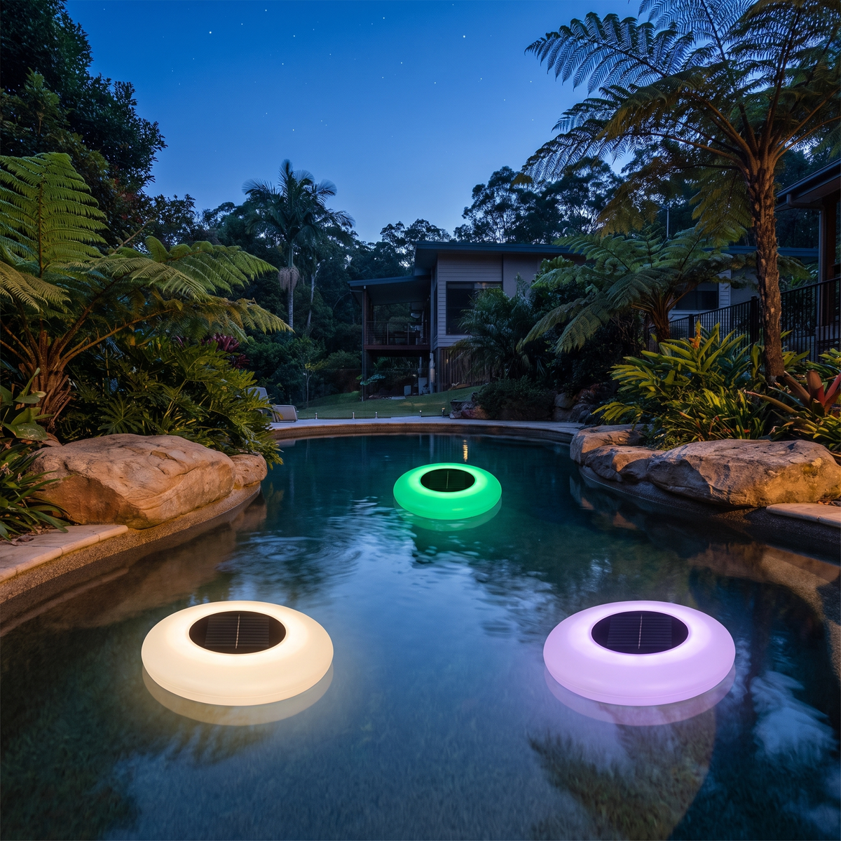 Three Agua floating solar pool lights glowing in a rock-edged freeform pool with ferns at dusk