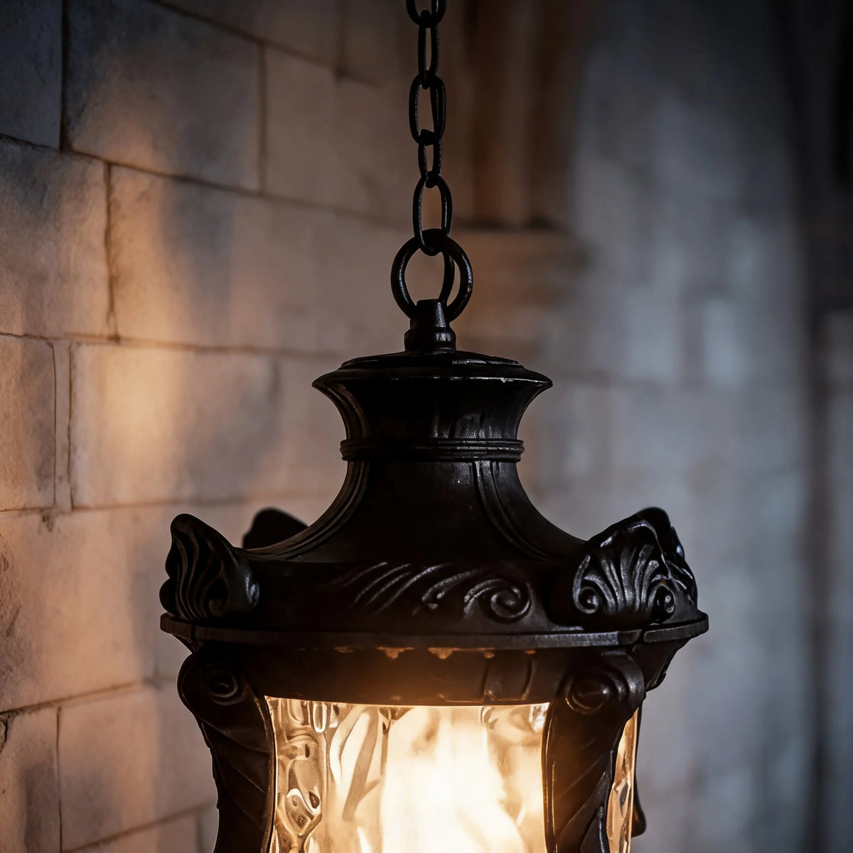 Close-up of the Anita lantern's scrolled aluminium cap and rippled glass glowing warm against a brick wall