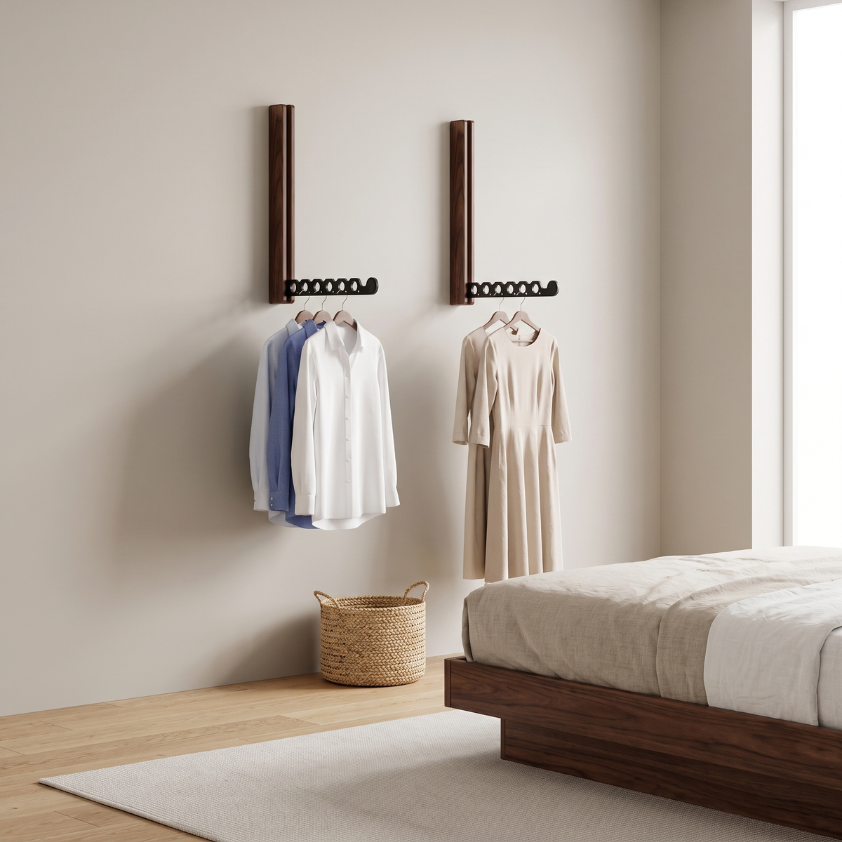 A set of two Arnie timber hanger rails in black walnut holding shirts and a dress beside a platform bed