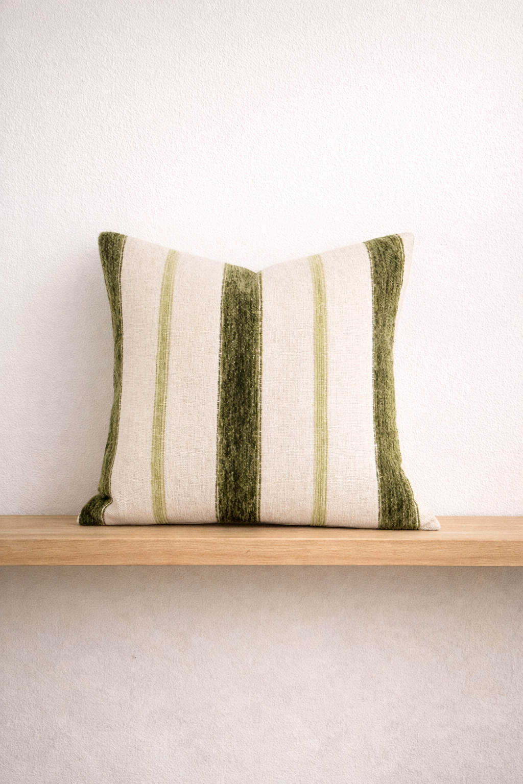 Banks green striped linen and velvet throw pillow on an oak wall shelf against a white wall