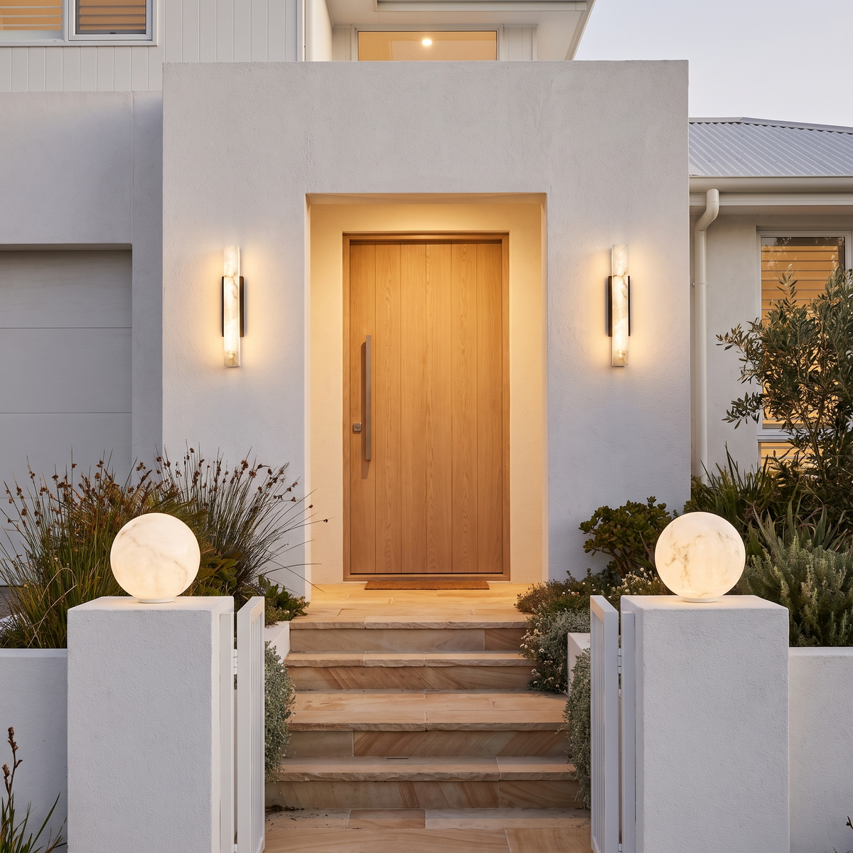 Pair of Zali marble effect wall lights at a beach house front door with Ulu moon pillar lights on the gate pillars