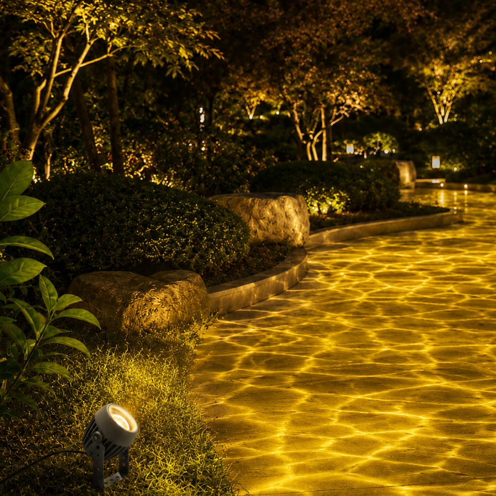 Beso outdoor spotlight projecting a golden yellow water ripple effect across a garden path at night
