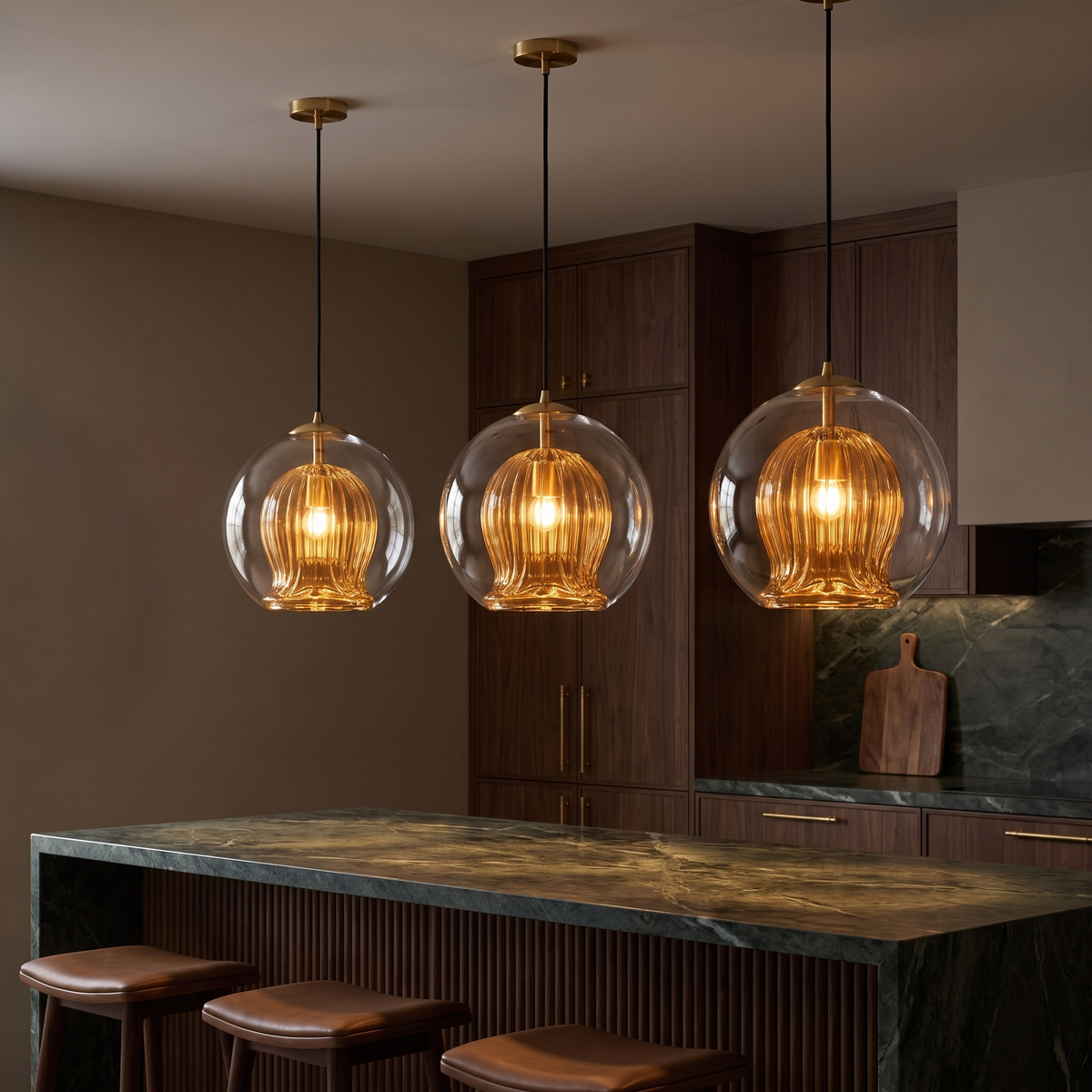 Three Capri amber glass pendant lights glowing over a green marble kitchen island at night