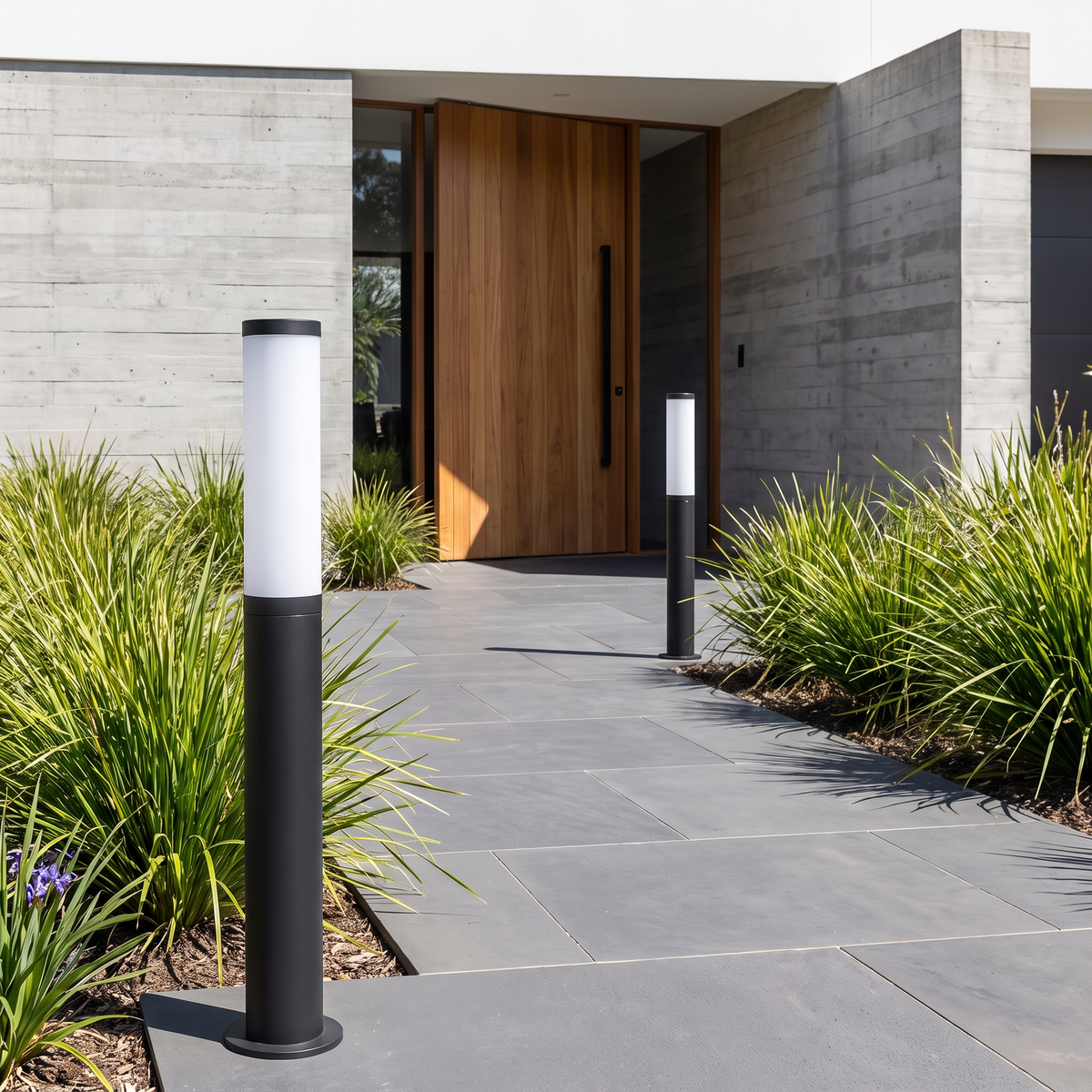 Two 78.7cm Clancy waterproof bollard lights along a charcoal paver entry path of a concrete home by day