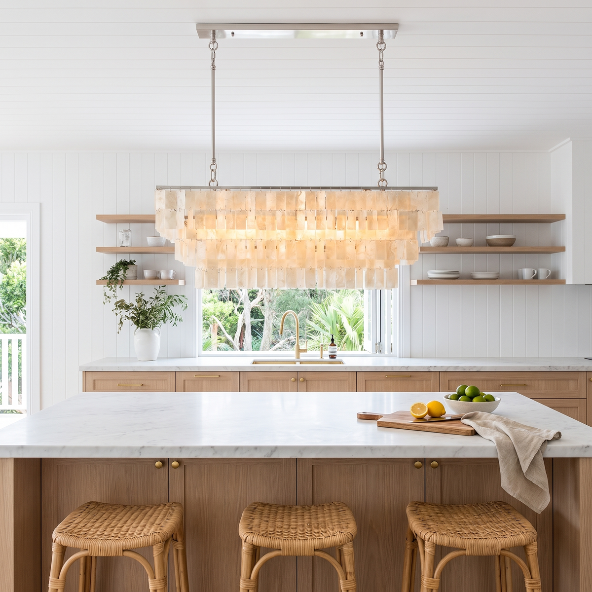 Coolum shell chandelier running the length of a marble island with rattan stools in a beach house