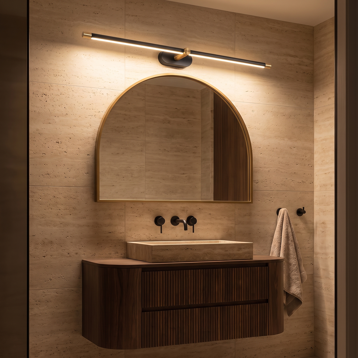 Debi black and gold wall lamp glowing above an arched mirror in a travertine ensuite