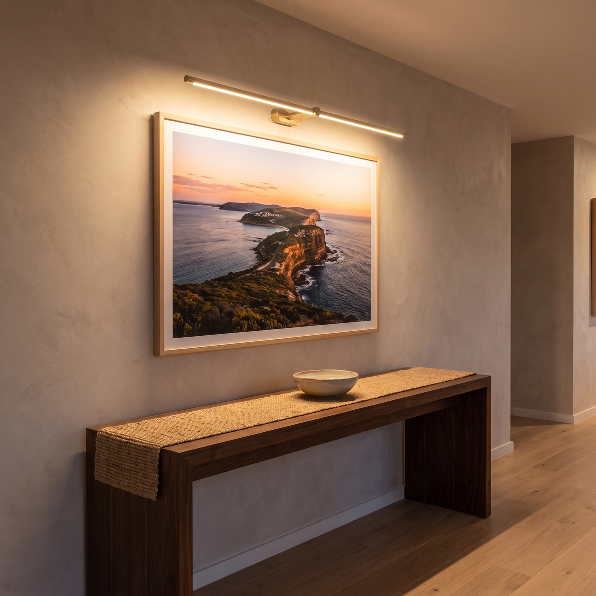 Debi gold wall lamp used as a picture light over coastal artwork above a walnut console