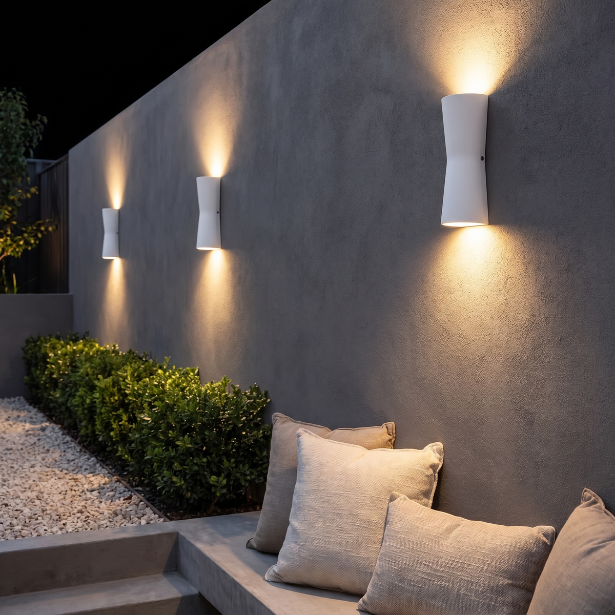 Three Dewy torch-style outdoor wall lights in white glowing on a charcoal courtyard wall at night