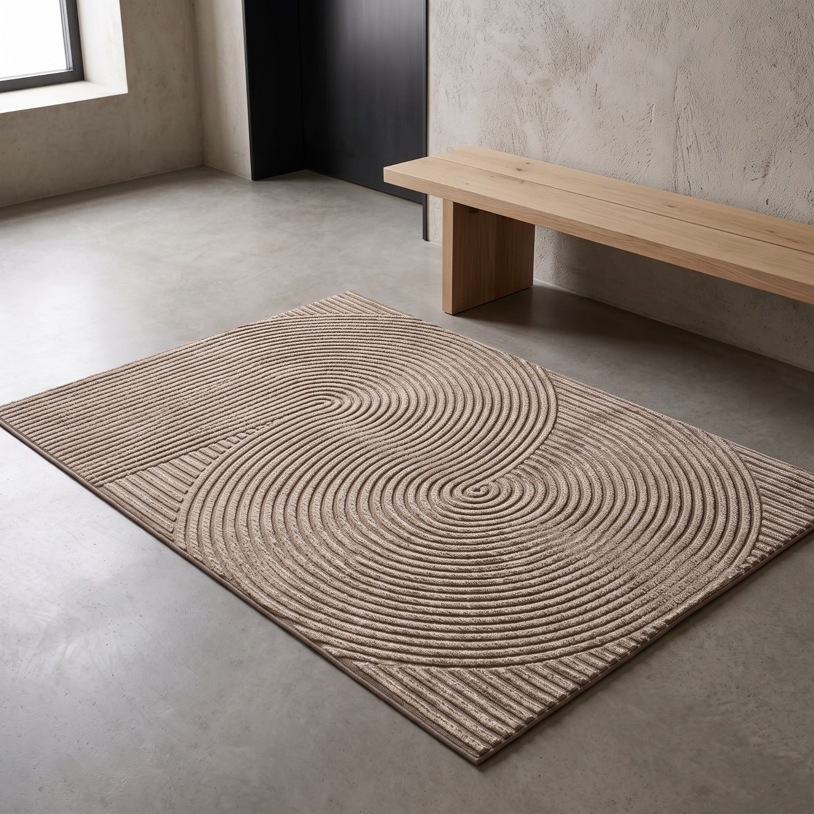 A rectangular area rug with a textured concentric circle pattern in beige and brown tones, styled on a concrete floor next to a minimalist wooden bench.