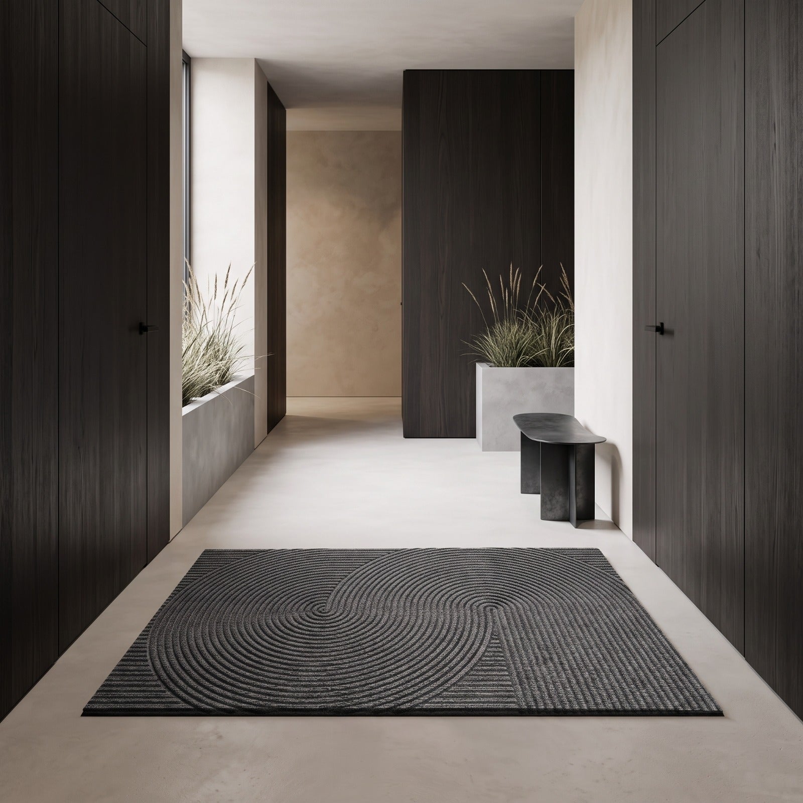 A dark gray rectangular area rug with a concentric circular wavy pattern, displayed on a light concrete floor in a modern minimalist hallway with dark wood doors and plants.