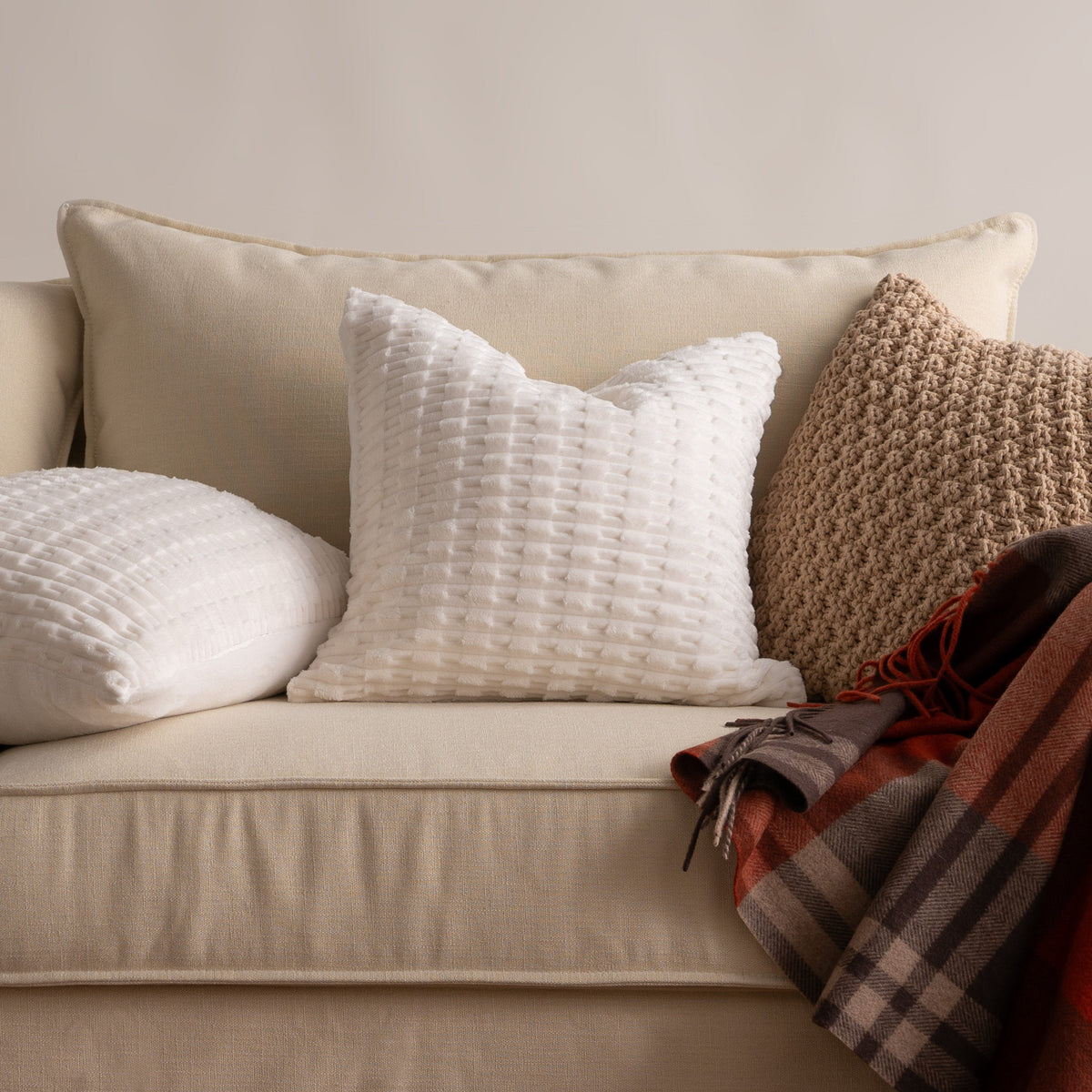 Faux fur pillow cover in winter white on a linen sofa with a tan knit cushion and plaid throw