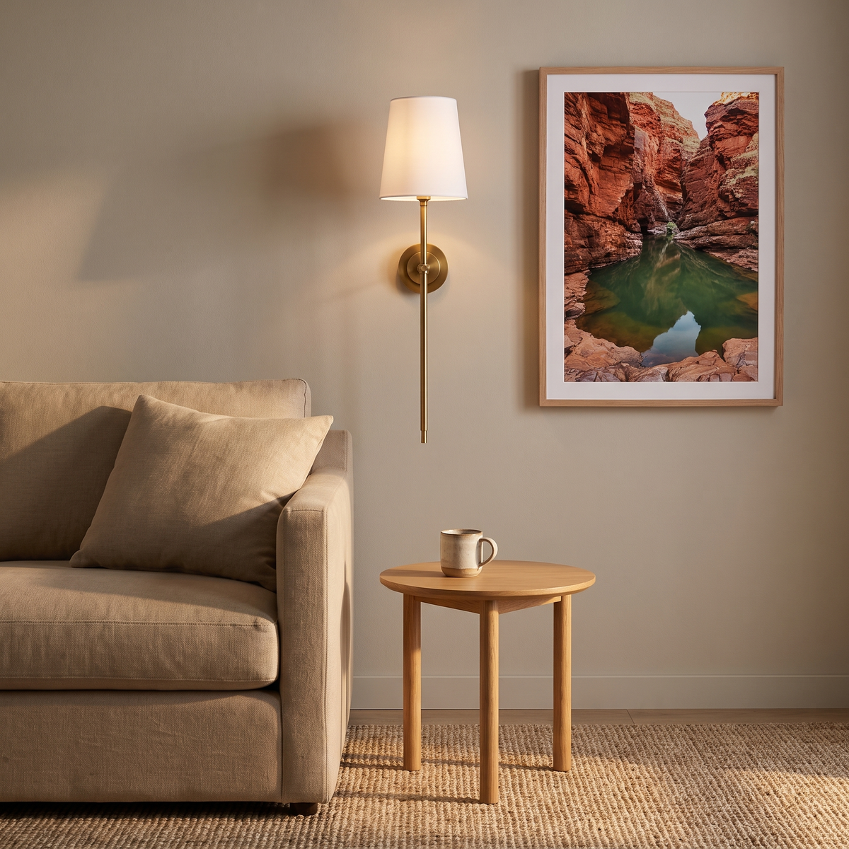 Tall Gini brass candlestick wall sconce with white fabric shade beside a linen sofa