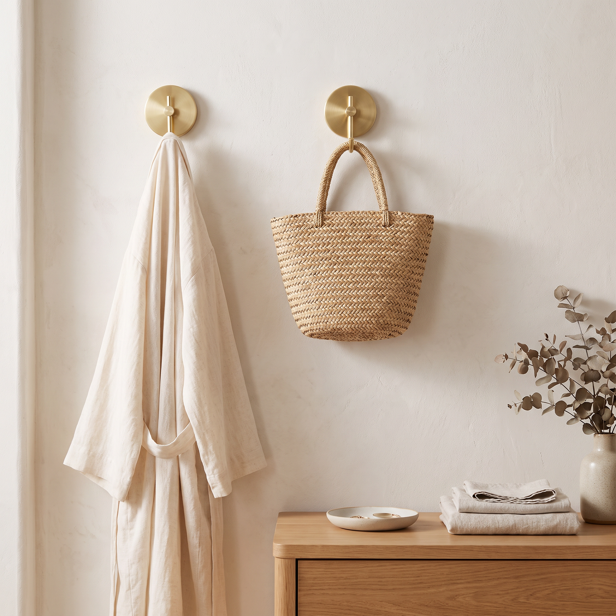 Capi Golden Hook brushed brass round wall hook in a dressing nook with a linen robe and straw bag