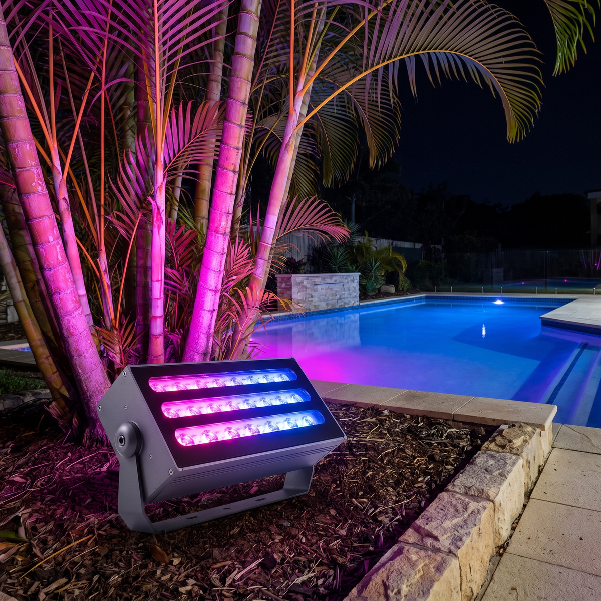 Honnibal RGB LED flood light washing golden cane palms in magenta and blue beside a resort-style pool