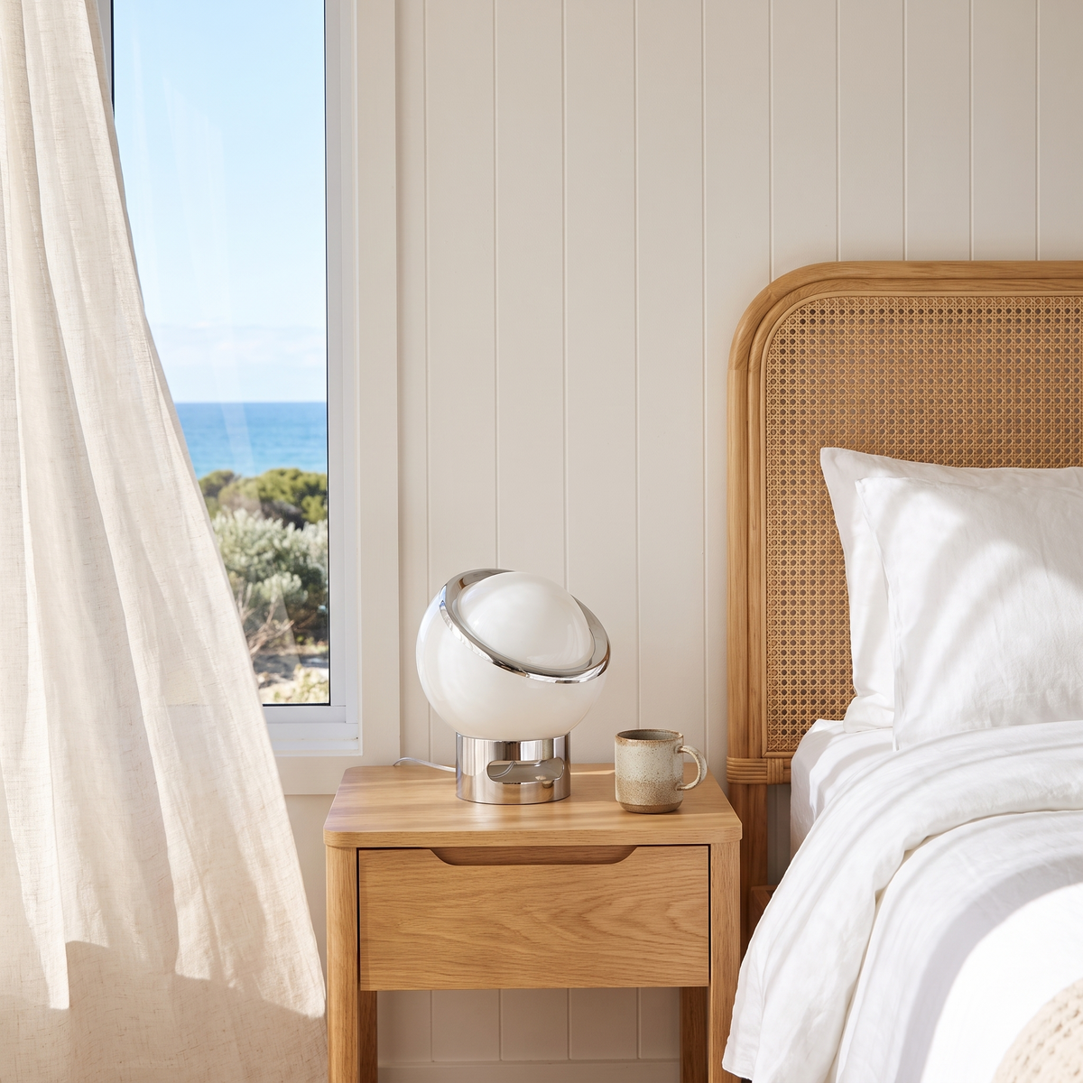 Jayla Bauhaus table lamp in white on an oak bedside table in a coastal beach house bedroom