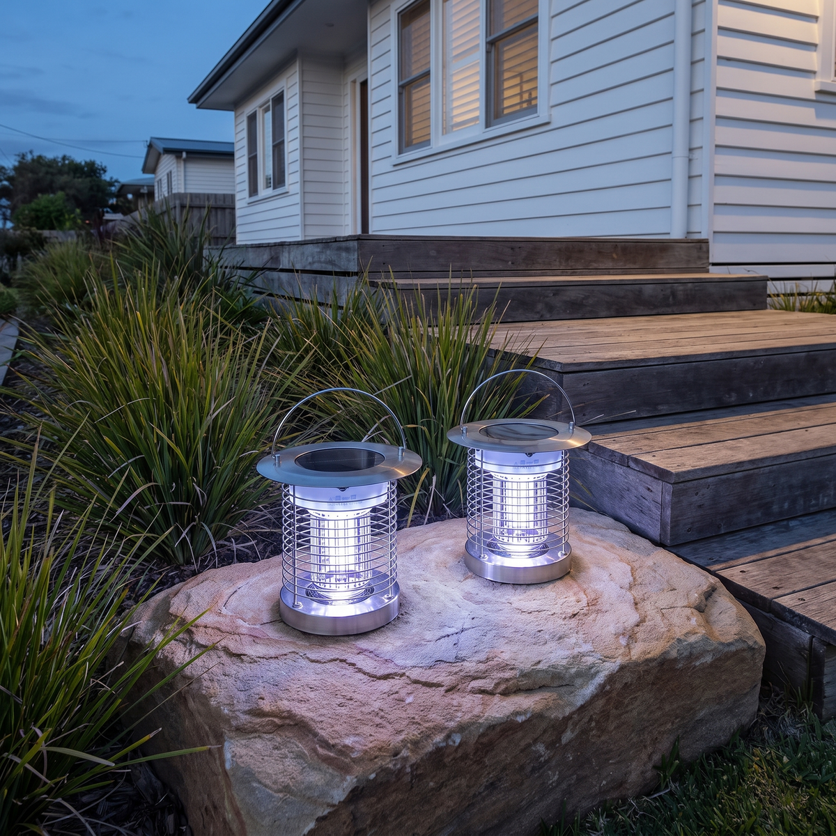 Two portable Juli Solar Bug Zapper Lights in silver on a sandstone boulder by beach house deck steps at dusk
