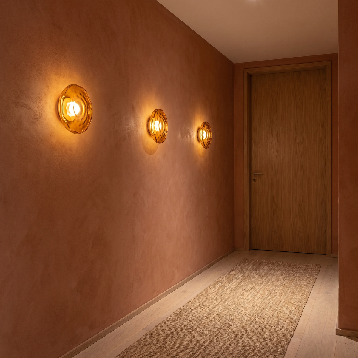 Three Kevi amber ripple glass flush round wall lights glowing along a terracotta hallway