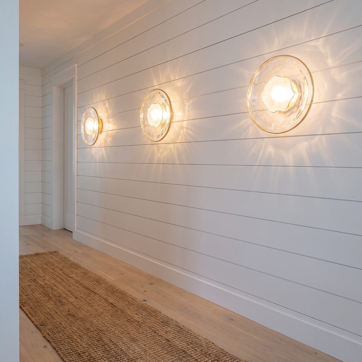 Kevi clear ripple glass round wall lights with gold rim along a coastal hallway