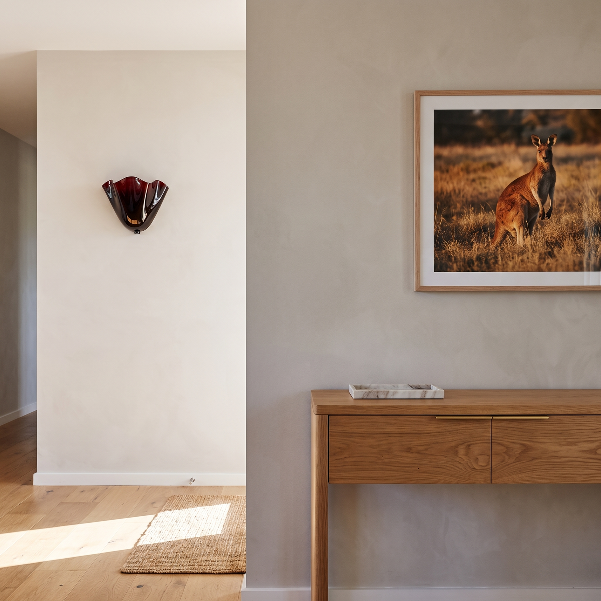 Kira artistic wall sconce in burgundy glass on a greige plaster wall above an oak entry console