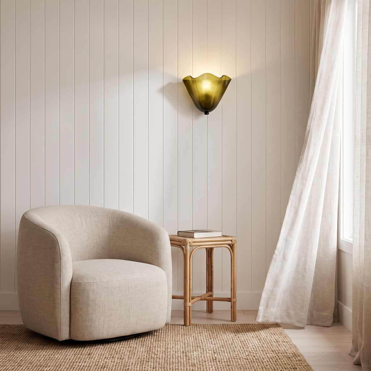 Kira artistic wall sconce in green glass lit beside a linen armchair in a coastal reading nook