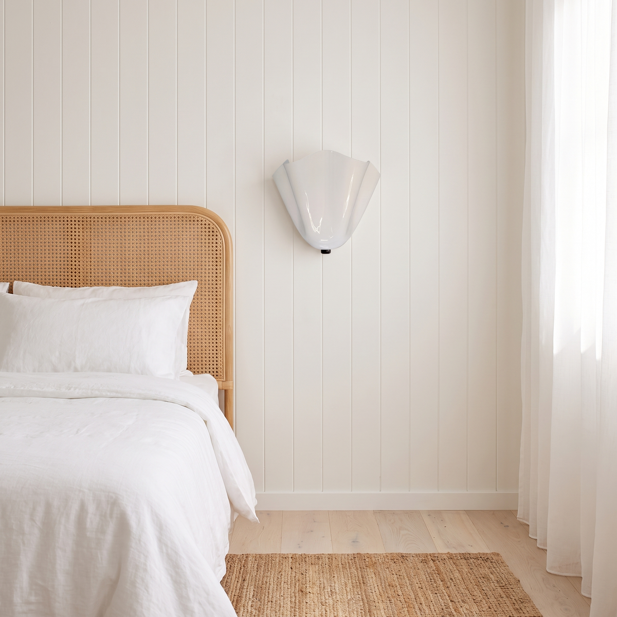 Kira artistic wall sconce in white glass beside a cane bedhead in an Australian beach house bedroom