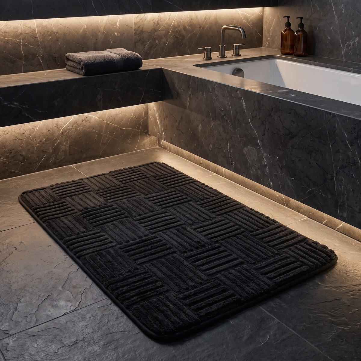 Marden striped non-slip bath mat in black on a dark stone floor beside a lit bathtub