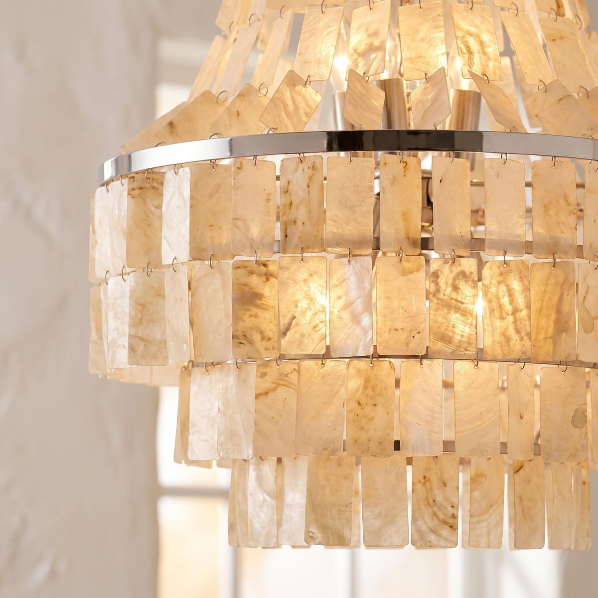 Close detail of the Maui chandelier's overlapping capiz shell tiles and chrome band glowing warm