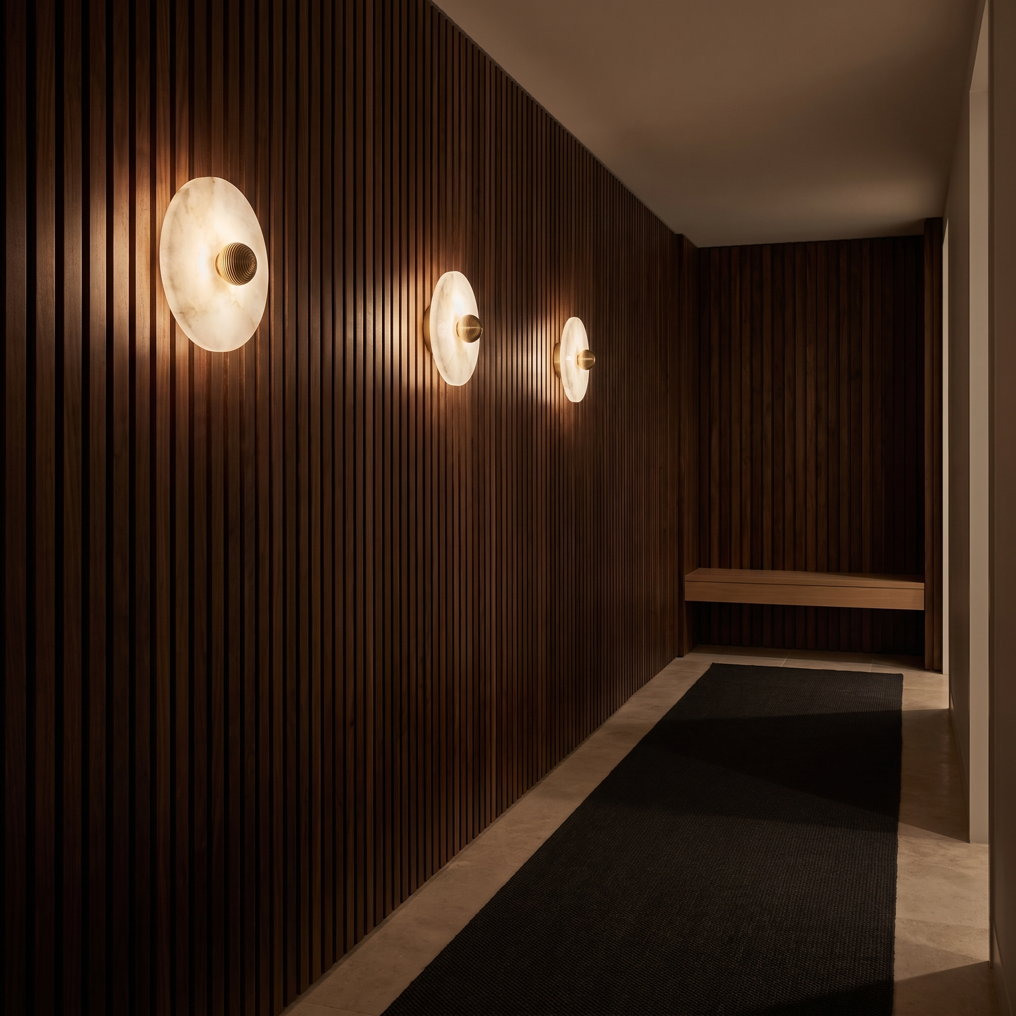 Row of three Miki round alabaster wall lights along a dark walnut hallway at night