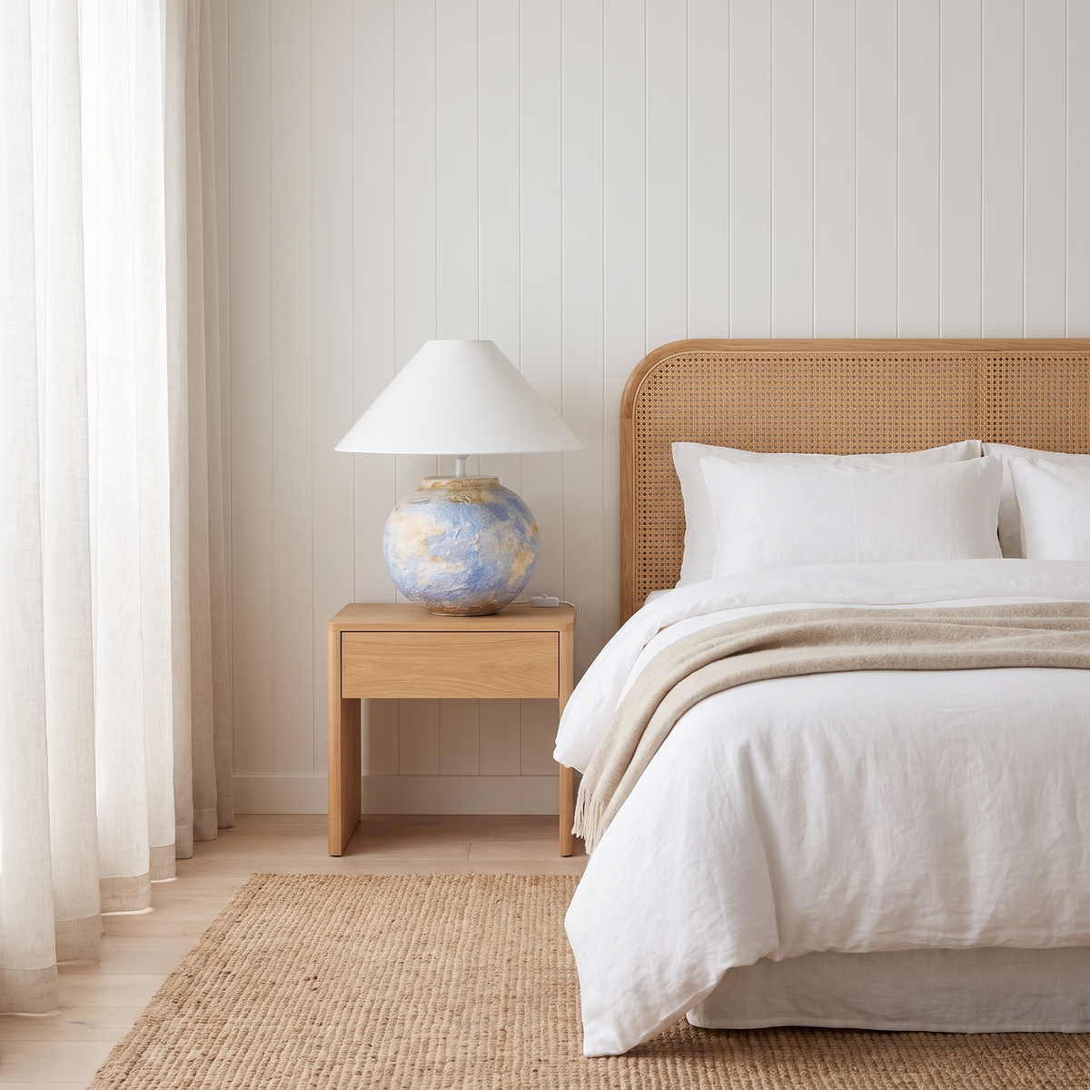 Monique Table Lamp with Watercolor on a bedside table in a coastal bedroom with a cane bedhead
