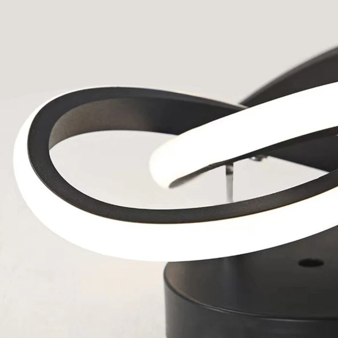 Monni LED ceiling light shown installed, with its illuminated looping arms lit against the ceiling