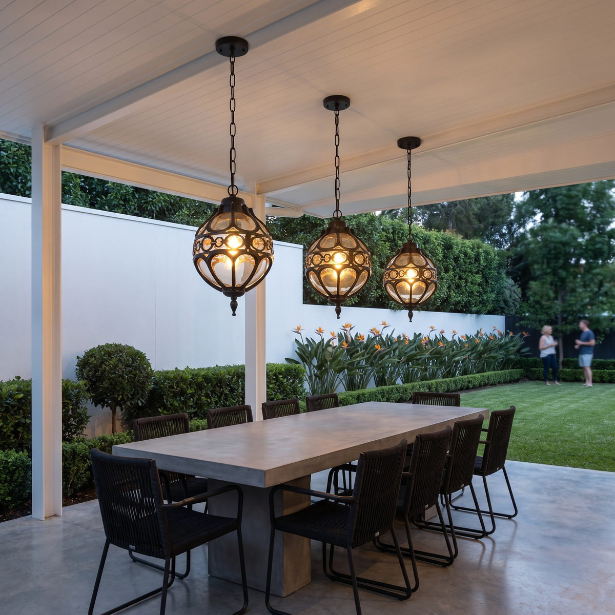 Three Olly black globe lantern pendants over a concrete table in a white dining pavilion at dusk