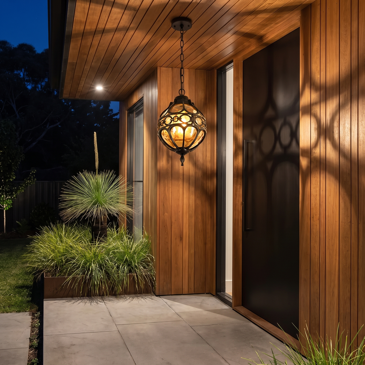 Olly outdoor pendant in black glowing above a pivot door with spotted gum cladding at night