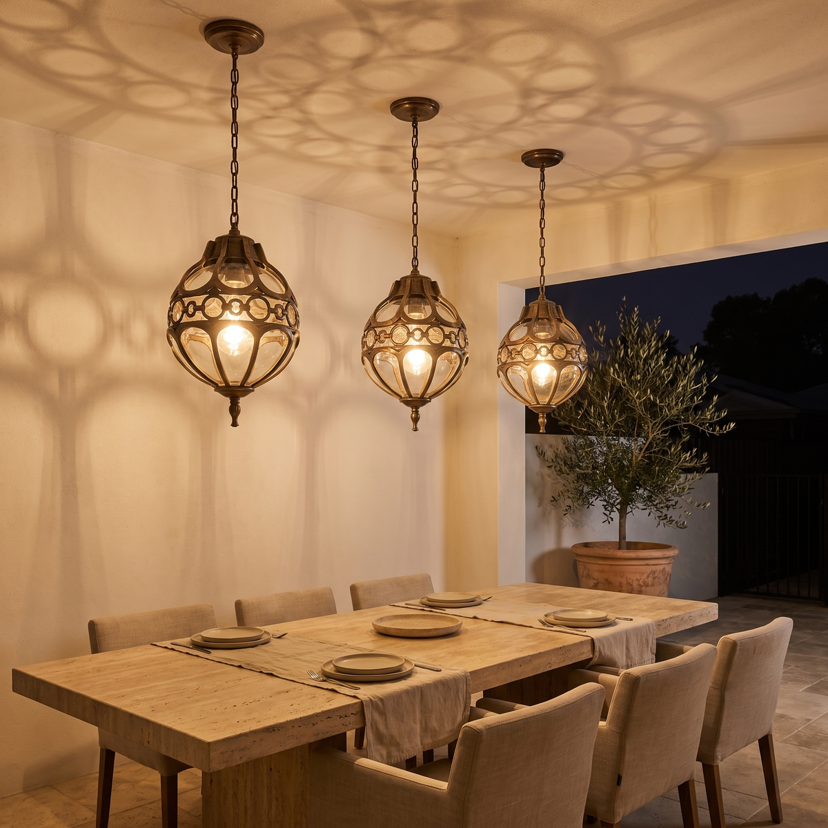 Three Olly outdoor pendants in bronze glowing over a courtyard dining table at night