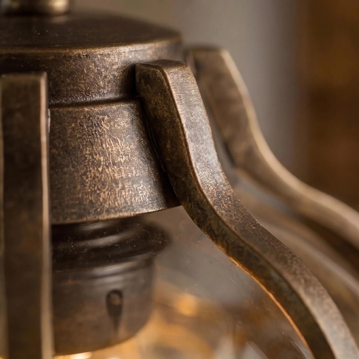 Close-up of the Olly pendant's textured bronze aluminium frame arms above the glass globe