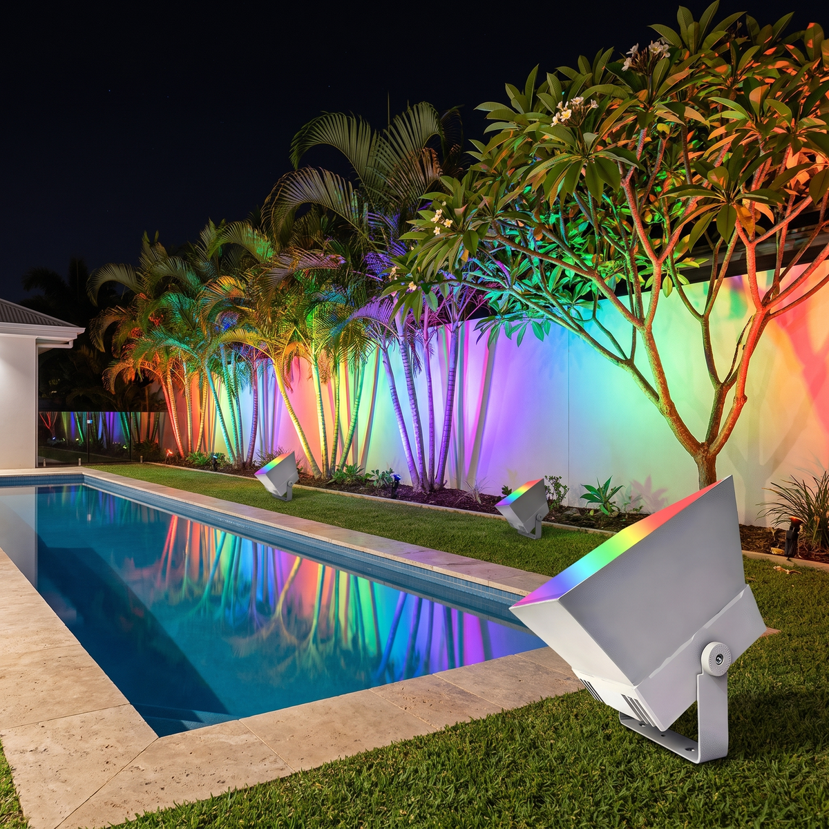 Oxford RGB outdoor spotlights lighting palms in rainbow colours beside a lap pool at night