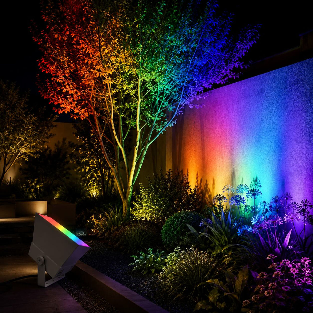 Oxford RGB outdoor spotlight in grey uplighting a garden tree and rendered wall in rainbow colours