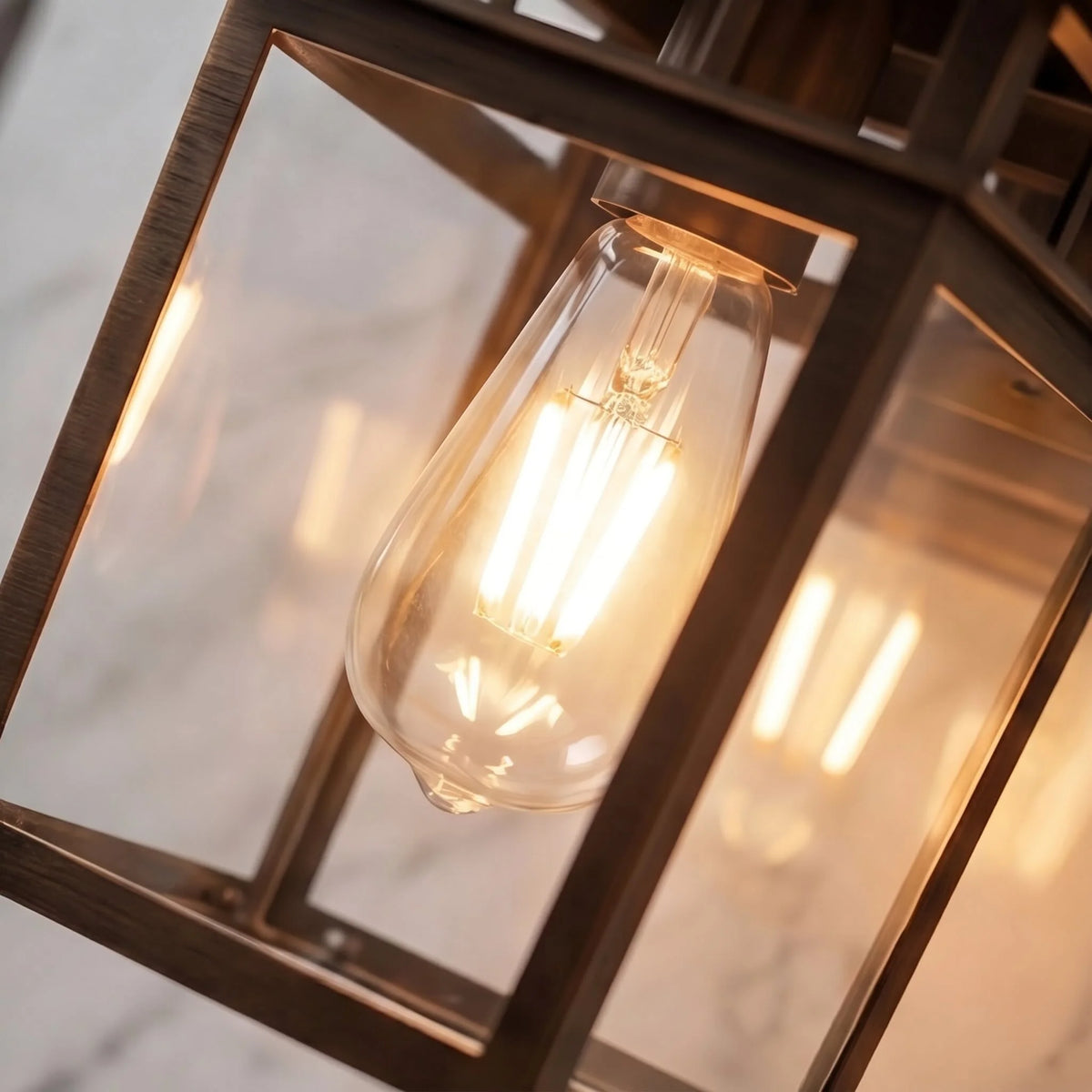 Close-up of the Pica retro wall lantern in bronze showing clear glass panels and a filament globe