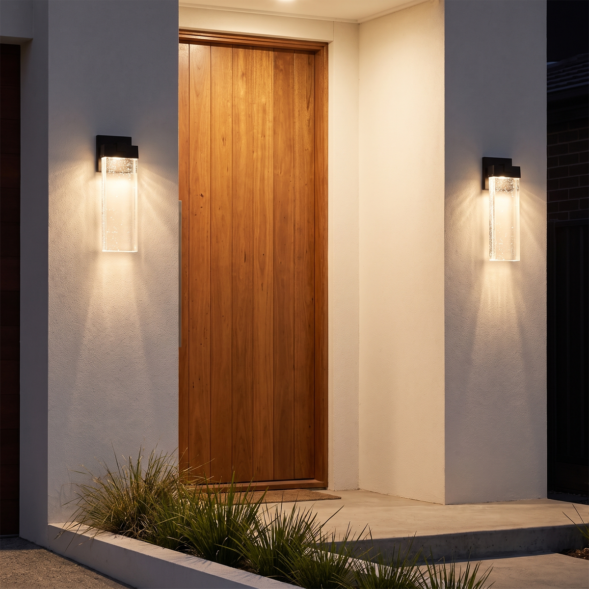 Two Poirier Outdoor Wall Lights in black flanking a spotted gum pivot door on a rendered home at night