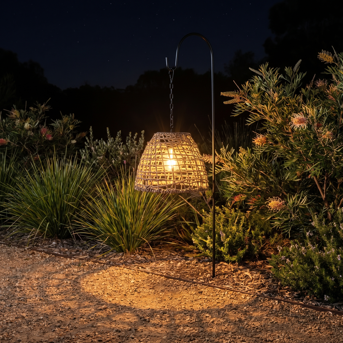 Riley rattan solar lantern on a shepherd's hook casting woven shadows over a native garden path
