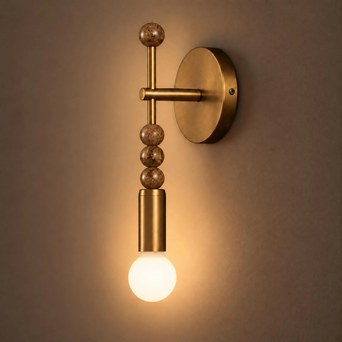 Sands antique brass wall sconce with brown marble beads lit against a warm wall