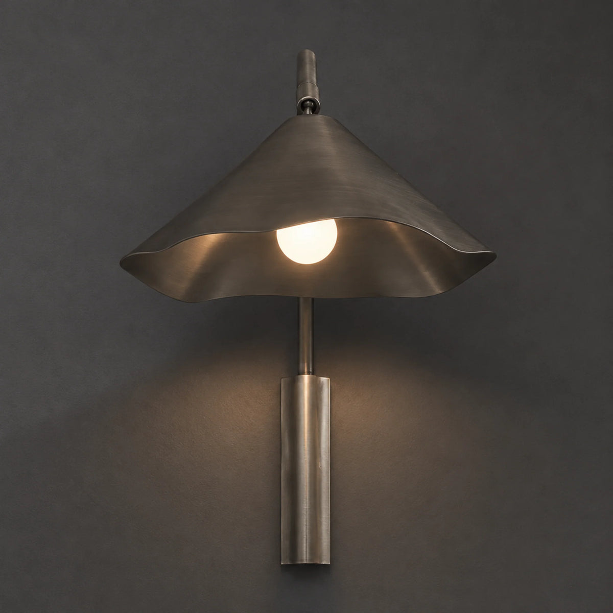 Sepo Arc wall sconce with its curved arm and fluted cone shade lit on a wall
