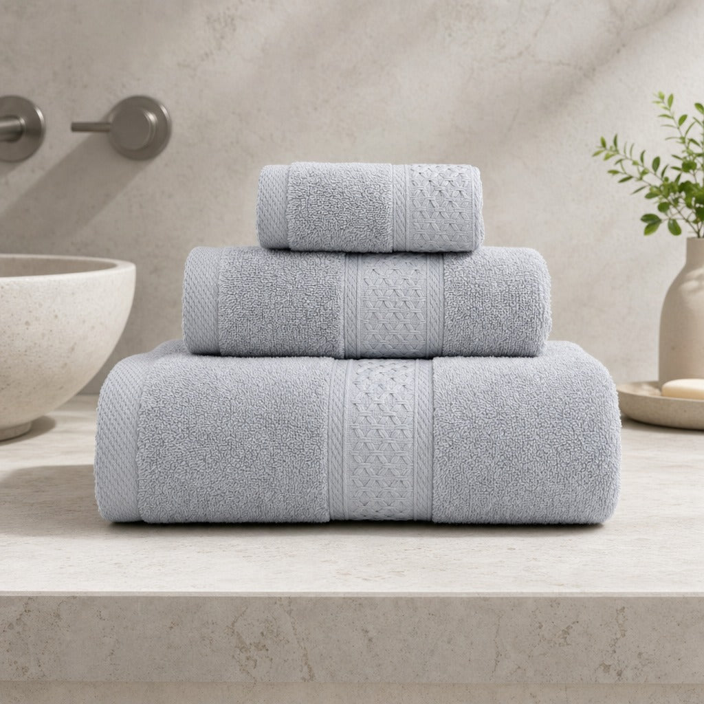 Serene 100% cotton bath towels in grey stacked on a stone bench beside a basin