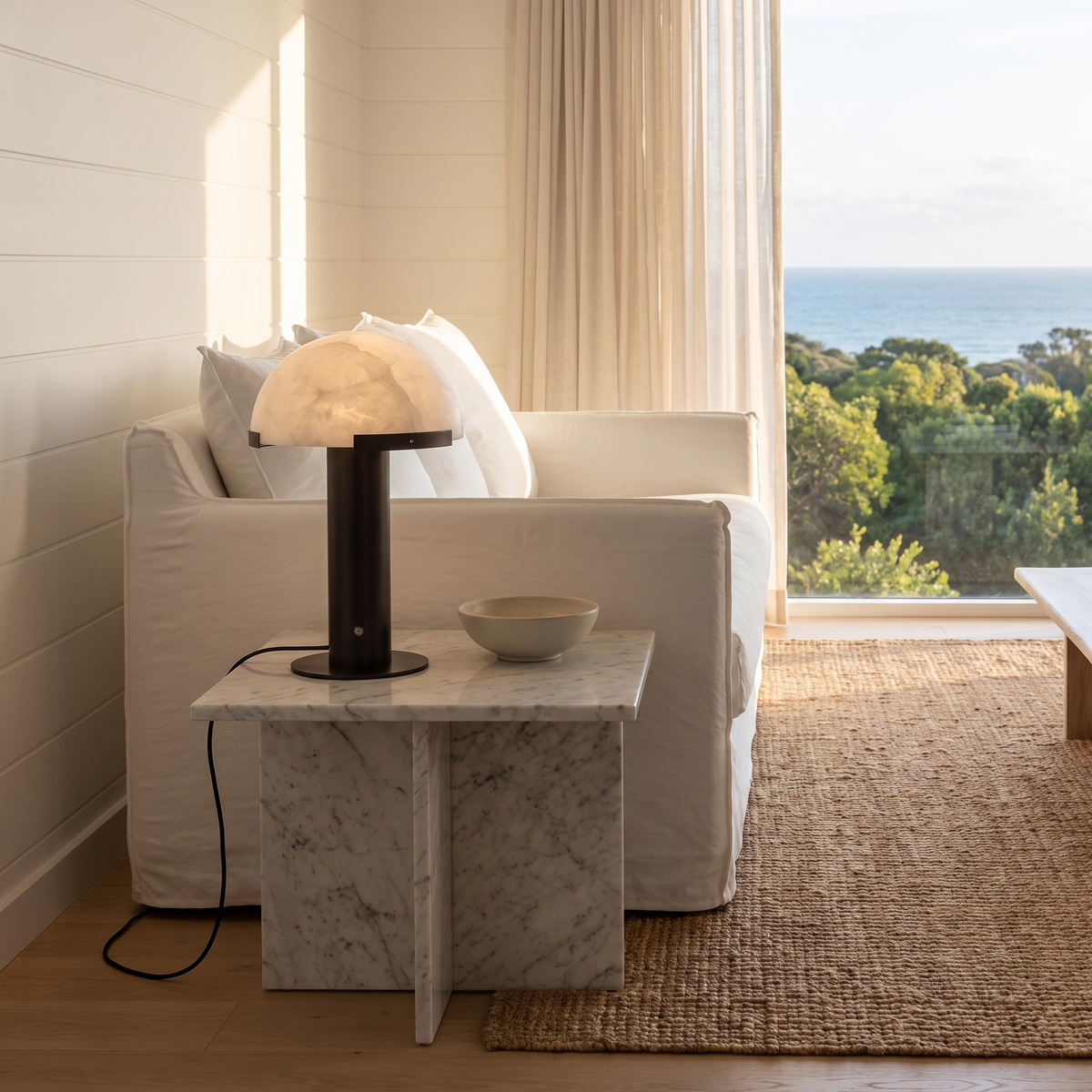 Taya alabaster table lamp with black bronze base on a marble side table in a coastal living room
