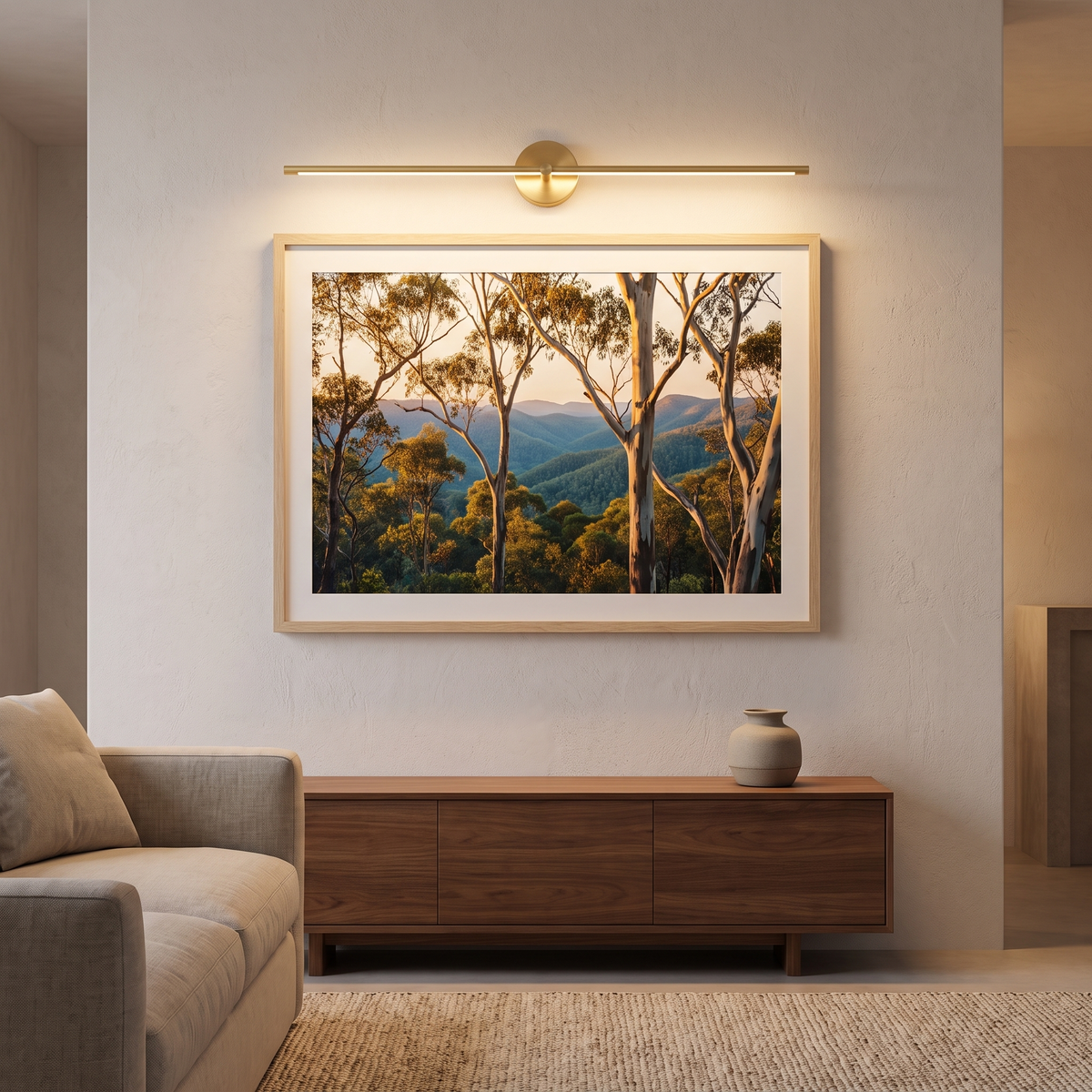Gold Tomi linear sconce lighting a framed landscape print above a sideboard in a Scandinavian living room