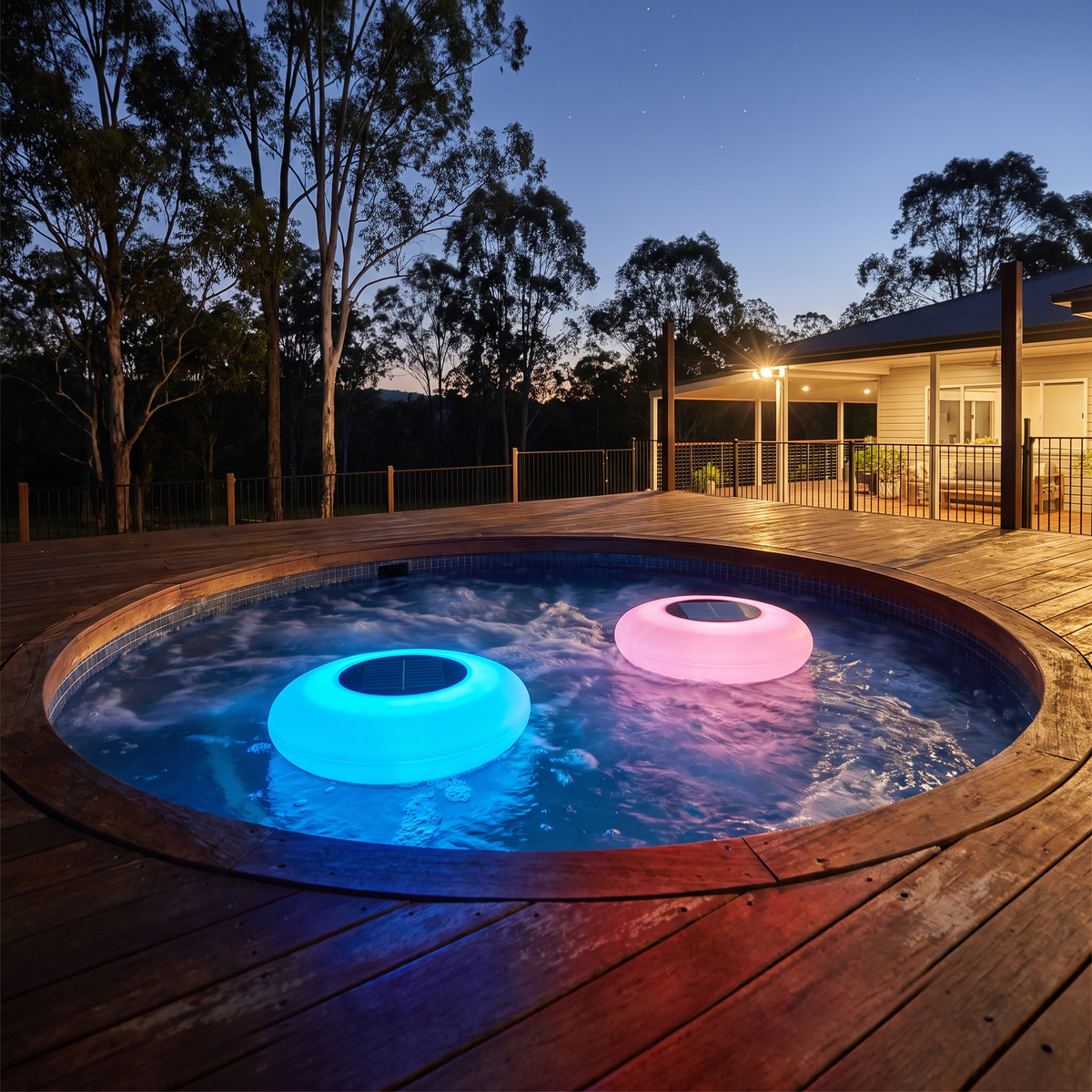 Agua floating solar pool lights glowing blue and pink in a round spa set in a blackbutt deck at night